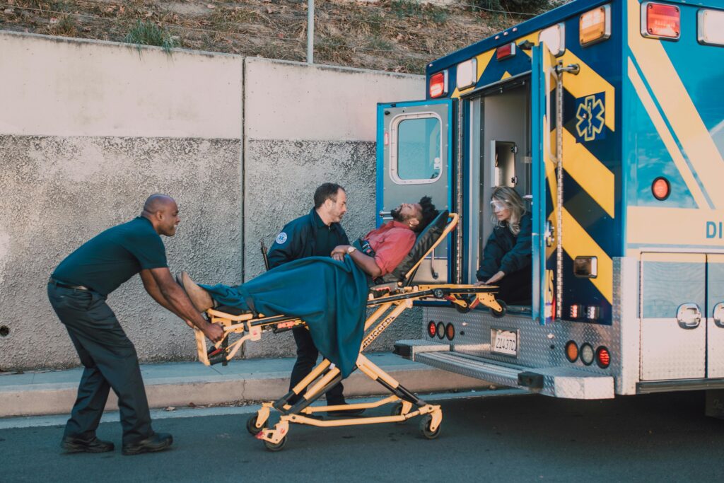 pexels-photo-6520084-6520084 First responders assist an injured man onto a stretcher and into an ambulance during a daytime emergency call.